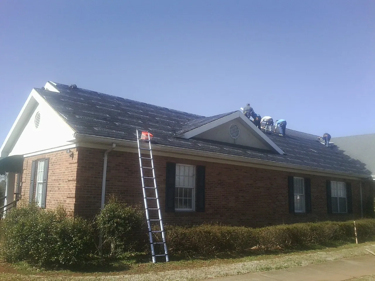 Crew tearing shingles off a brick ranch roof with a ladder set — Metal Roof Repair work by our crew in Nyack