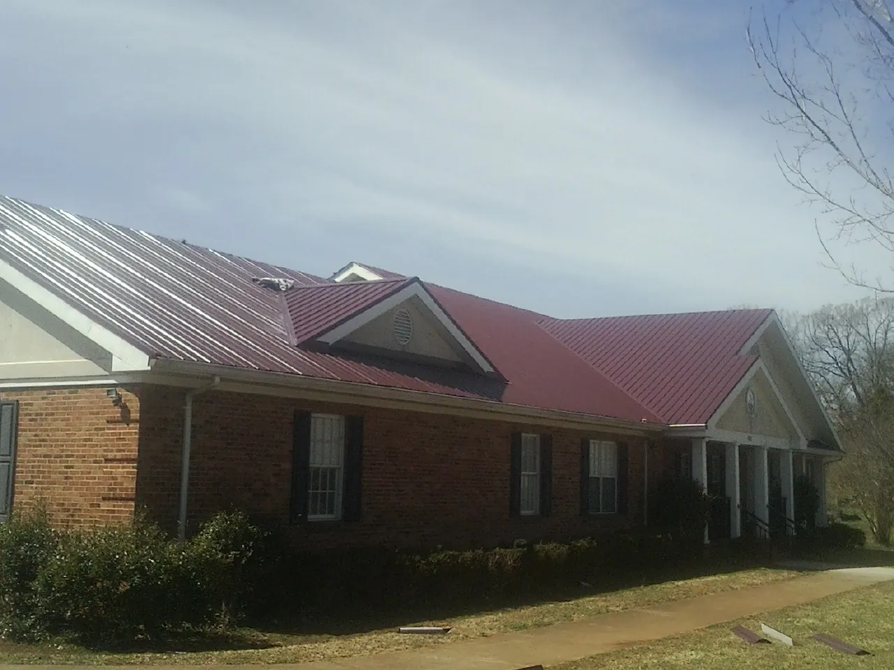 Red metal roof with gabled entries on a long brick building, from a Hail Damage Roof Repair job in Nyack