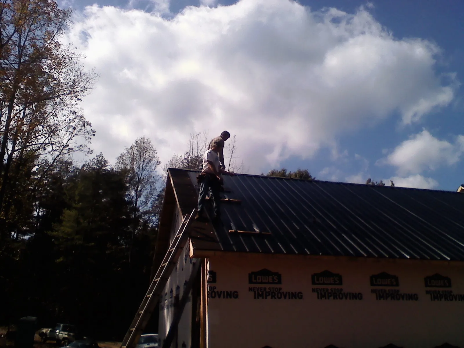 Roofer fastening dark metal panels high against a cloudy sky, from a Roof Inspection job in Nyack